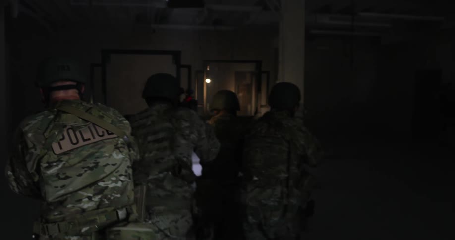 A police team holding shields is moving forward in a dark building
