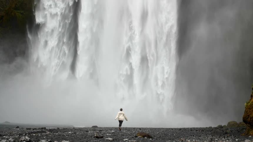 A person runs towards a large waterfall in the wilderness
