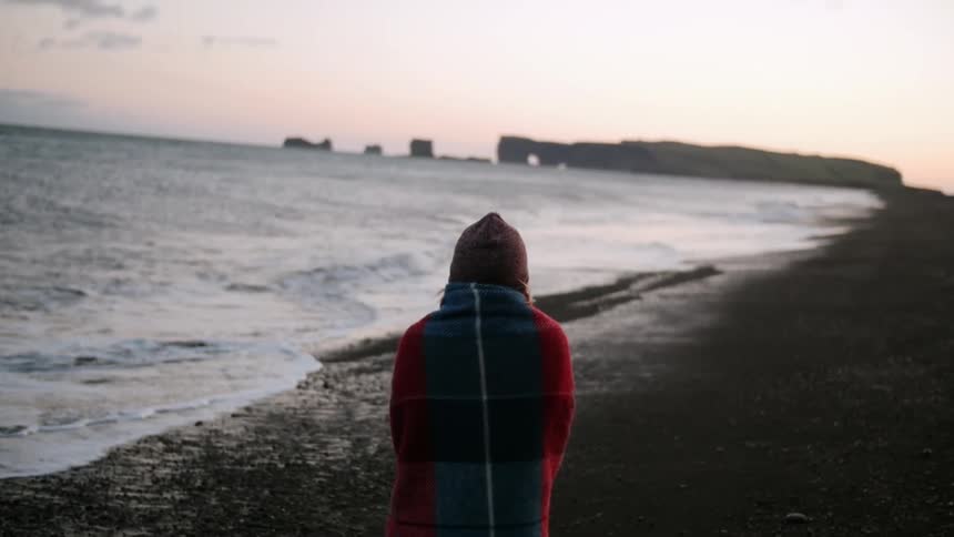 A woman walks on the beach at sunset
