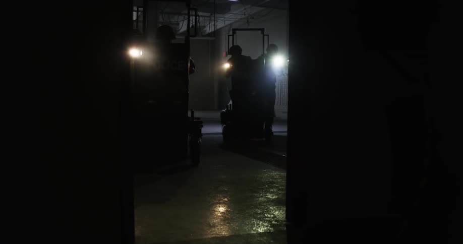 Police carrying shields are traveling towards a dark doorway