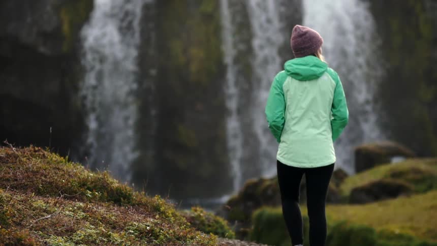 A woman walks towards a waterfall in the wilderness