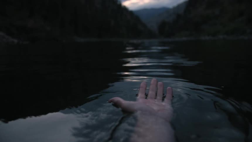 A hand is moving slowly in the water by some hills