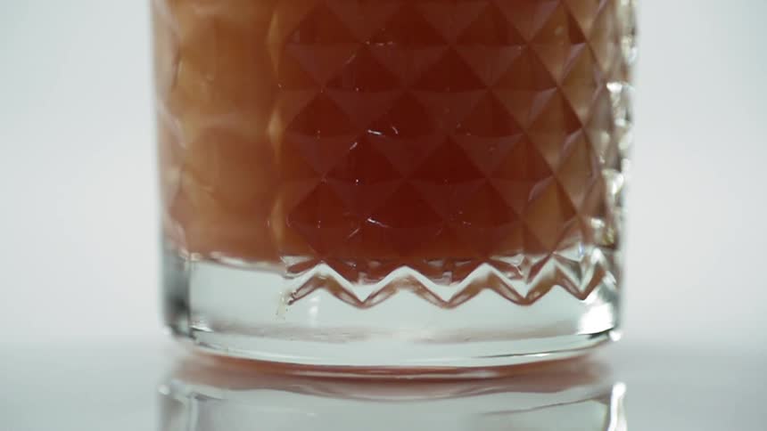 A stirrer moves through a glass filled with amber colored liquid