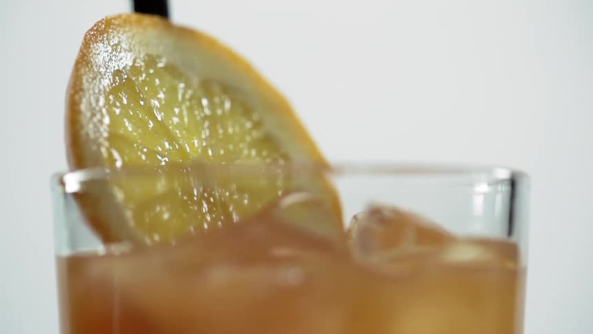 An orange slice is dropped into a glass containing liquor and ice