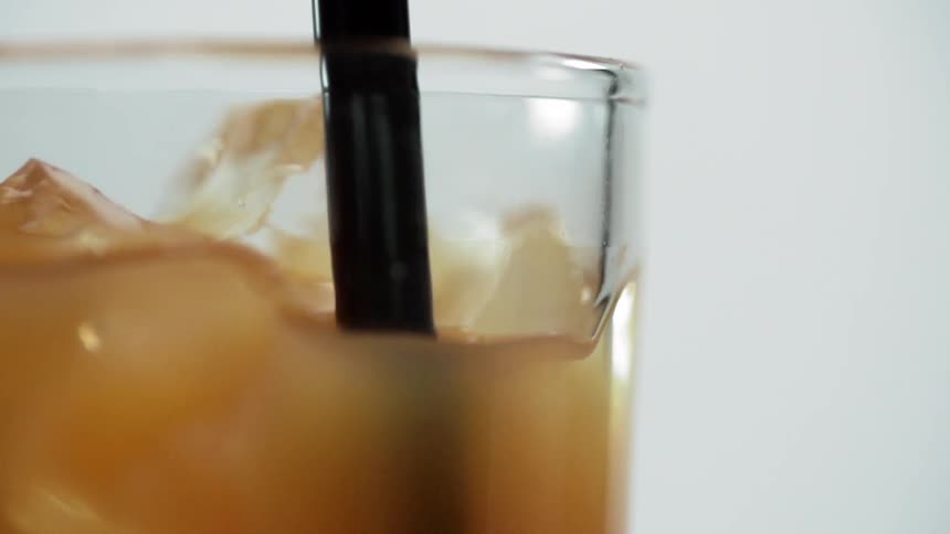 A straw is stirring a glass of liquids and ice