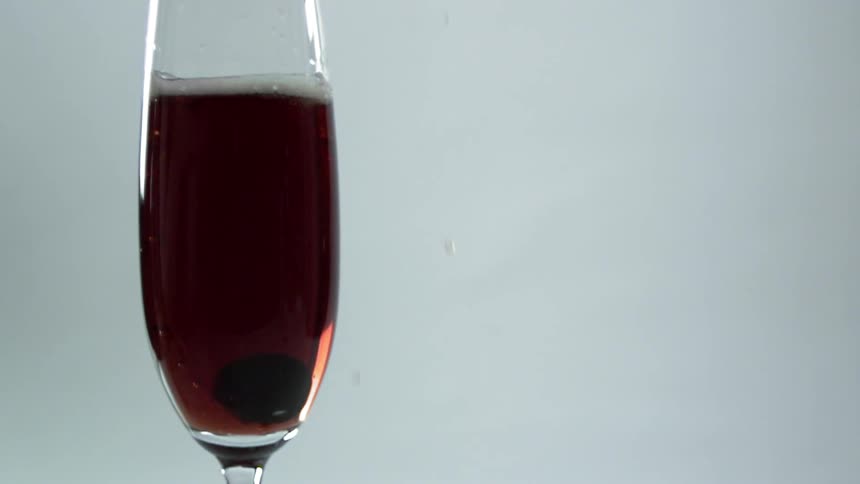 A berry being dropped in a glass of alcohol during a photo shoot