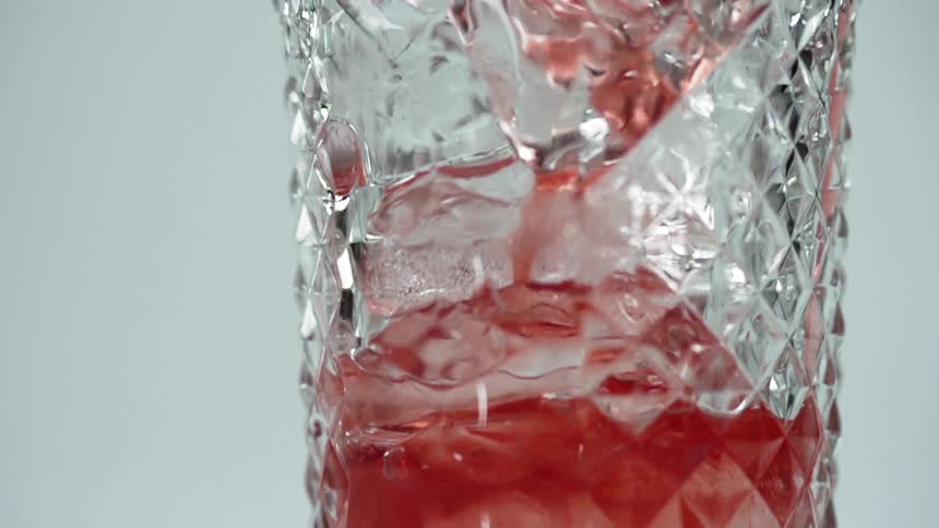 A glass with ice with red liquid being poured into it