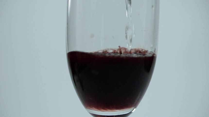 Clear liquid is being poured into a glass of red wine