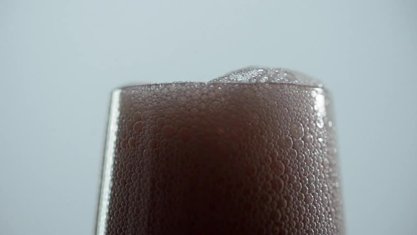 A colored drink in a glass foams up over the rim