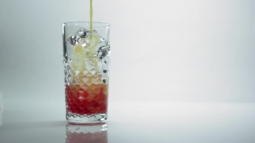 A yellow liquid being poured into a glass with ice and red liquid