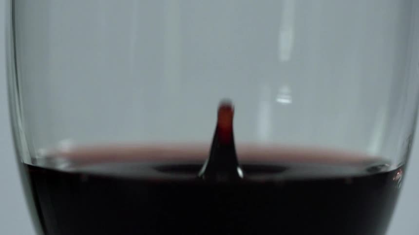 A drop of dark red liquid falling into a wine glass