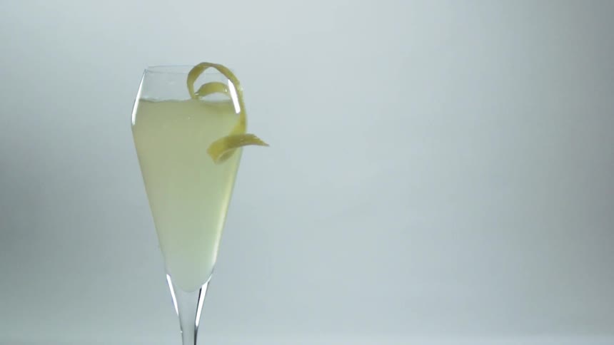 A curly lime rind garnish is dropped into a cocktail in a tall glass