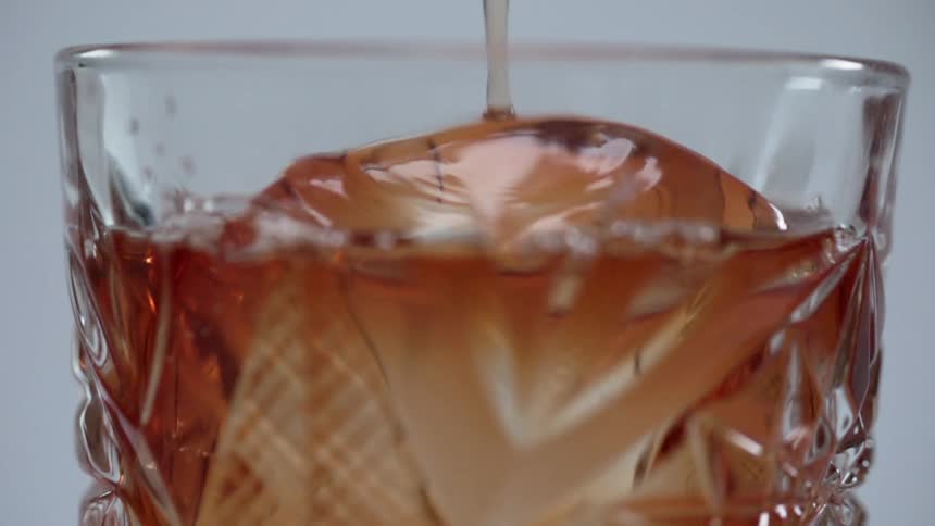 An amber liquid beverage is poured on top of ice in a clear glass