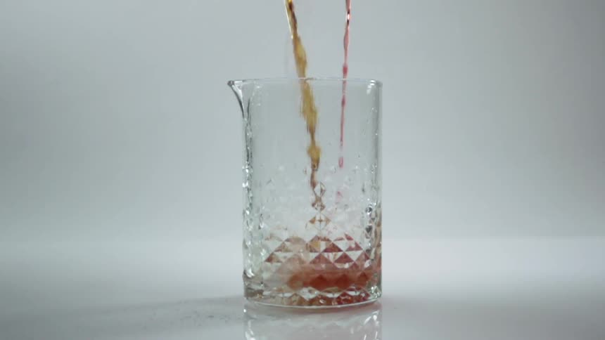 Two different colored liquids are poured into a faceted glass pitcher