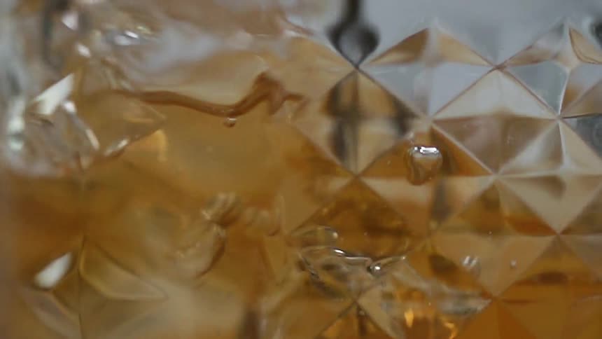 Ice cubes and an amber liquid are stirred in a clear glass