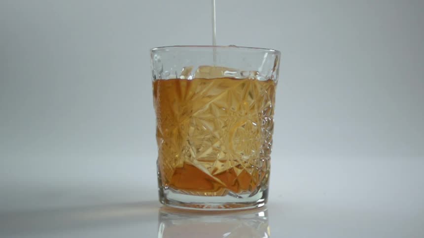 An amber liquid being poured into a glass of ice