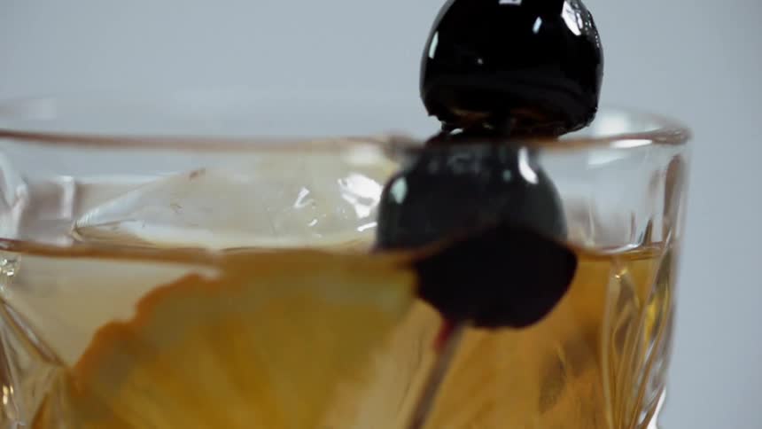Garnish on a toothpick is placed into a cocktail glass with ice and citrus slice