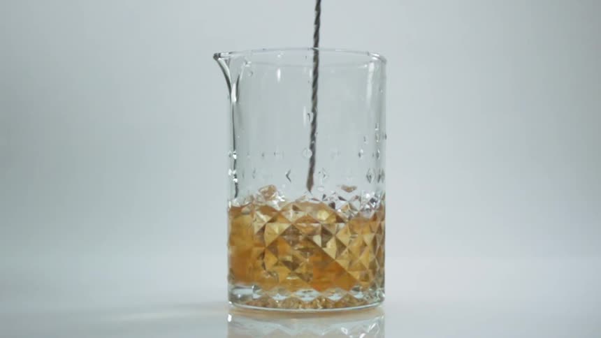 A glass of beer is being stirred with a spoon