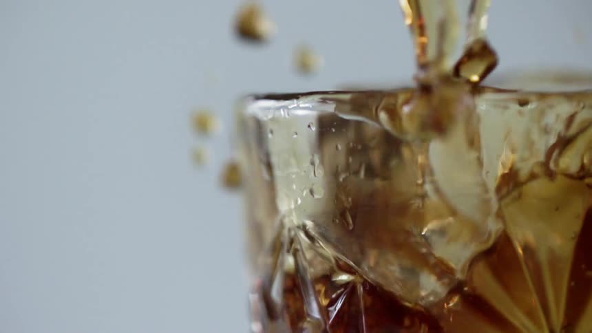 A large ice cube drops into a glass and splashes liquid around