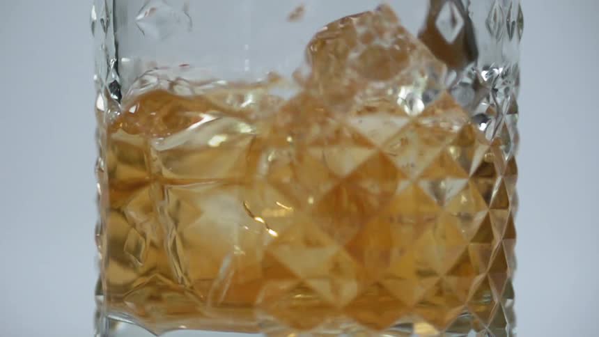 A spoon stirs ice cubes and amber liquid in a clear cocktail glass