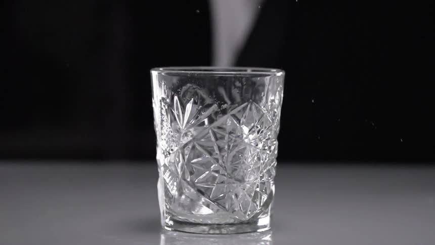 A person drops an ice cube in to a cocktail glass