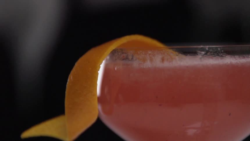 An orange peel is dropped in a cocktail glass containing red liquor
