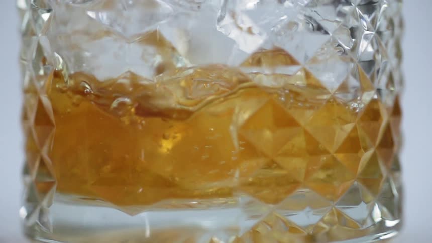 Amber colored liquor pours into a glass with ice cubes