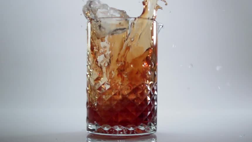Several ice cubes fall into a drink and splash the liquid around
