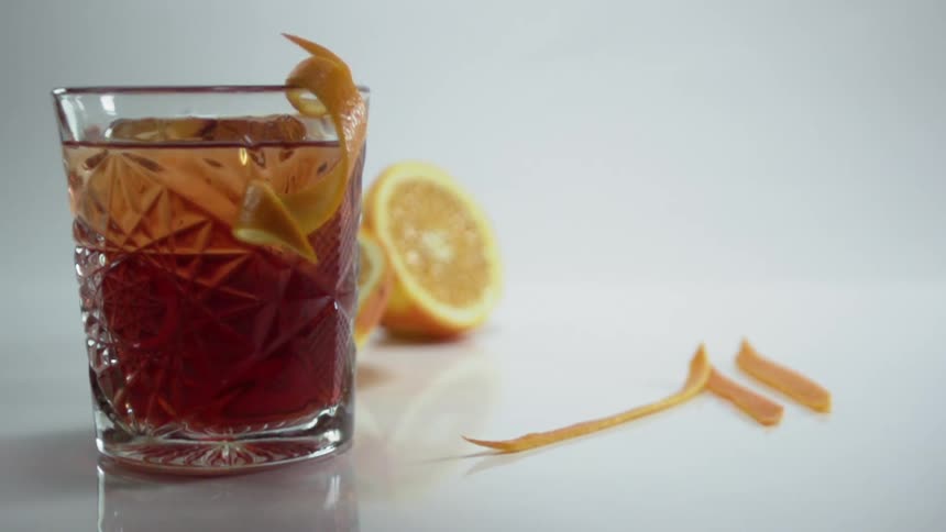 An orange peel falling onto the rim of a glass of old fashioned