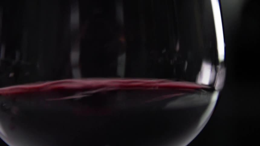 Drops of red wine are added to a wine glass already half filled
