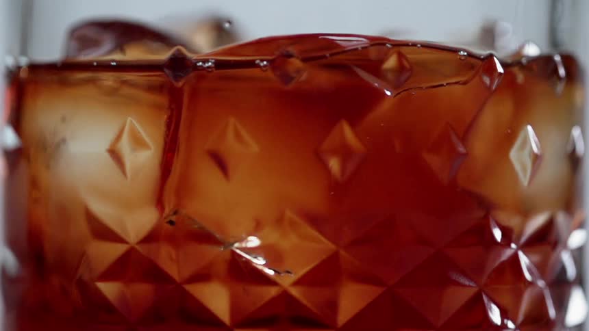 Ice slowly swirling in a glass of amber liquid