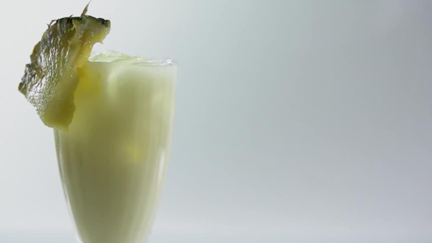 A piece of fruit drops and catches on the rim of a drink glass