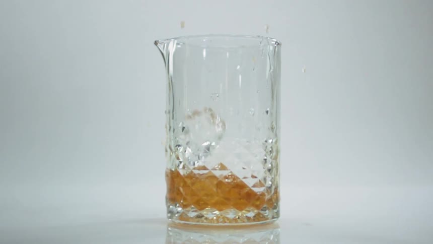 Ice falling into a pitcher of alcohol with a white background
