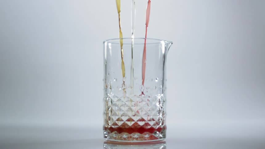 Three streams of liquid each a different colored being poured in a glass pitcher