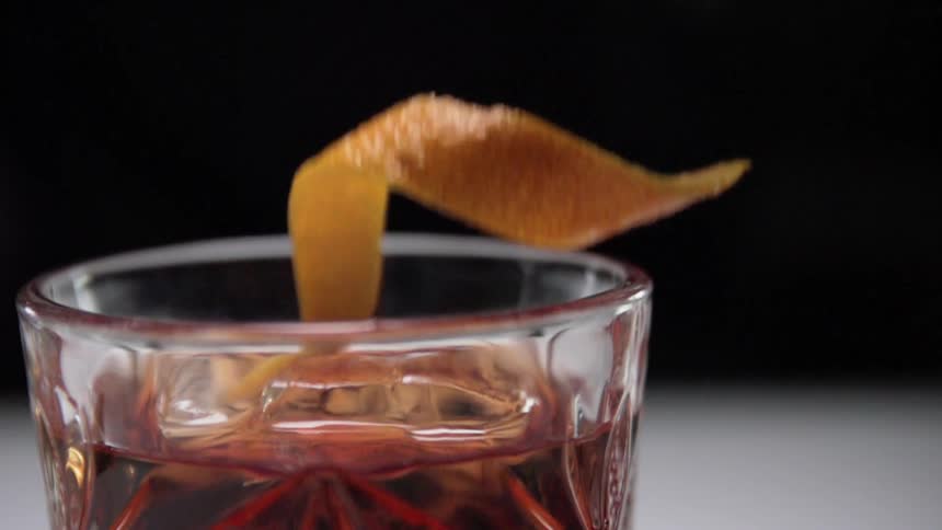 An orange peel is added to a cocktail in a glass