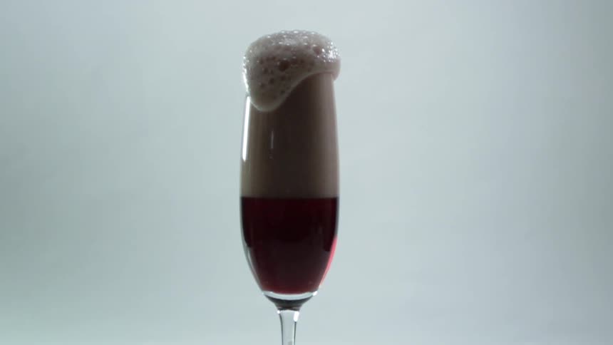 A champagne glass with red liquid and bubbles pouring out of it