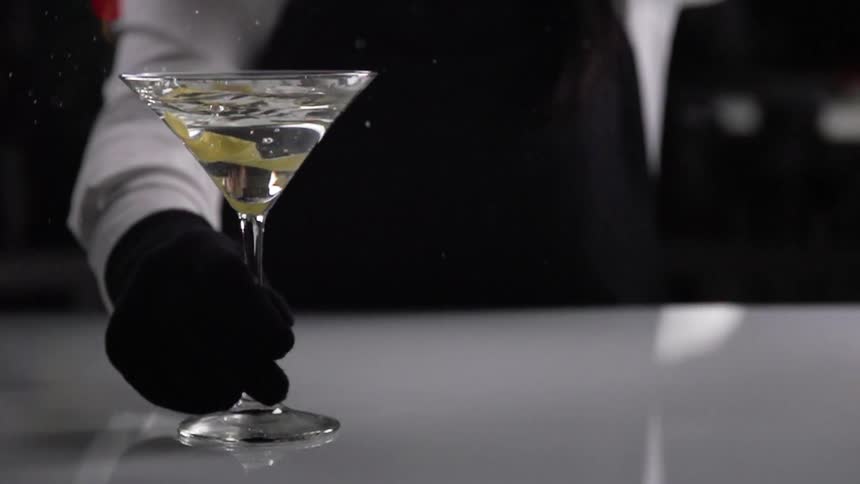 A bartender drops a piece of fruit peel into a martini