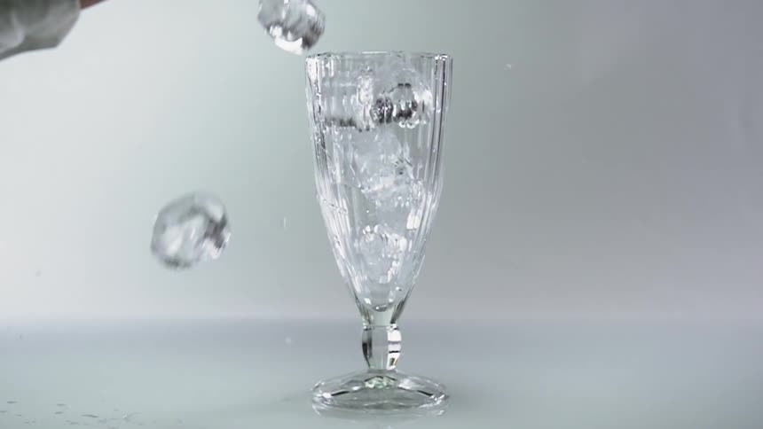 Ice falling into a glass with a persons hand in the background