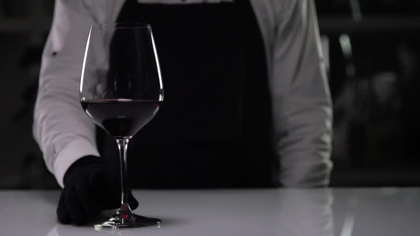 A bartender slowly slides a glass of red wine across a table top