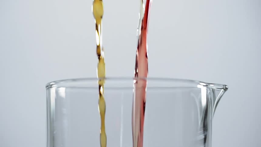A clear a red and a yellow liquid being poured into a pitcher