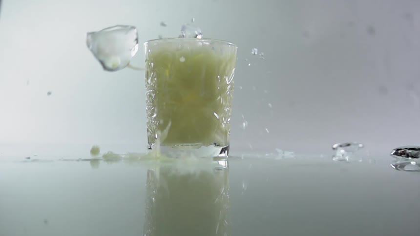 Ice cubes fall into a glass of cocktail