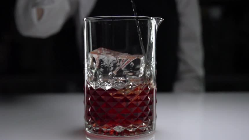 A bartender stirring ice and liquor in a glass pitcher with a stirring spoon