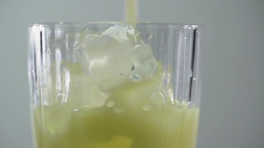 Yellow cocktail is being poured into a glass full of ice cubes