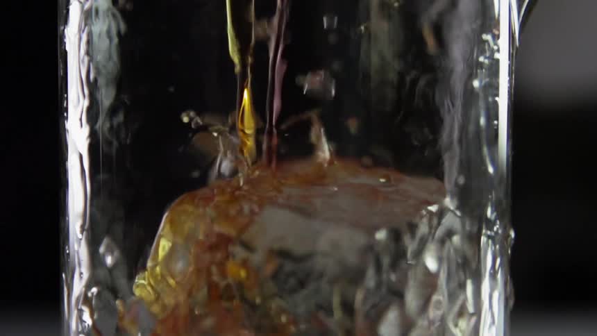 A yellow a red and a clear liquid being poured into a glass with ice
