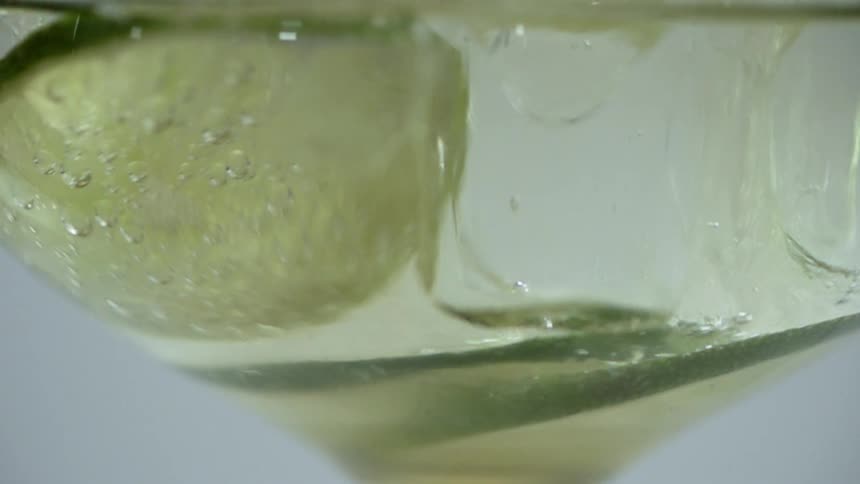 Carbonation bubbles rise to the top of a martini glass filled with liquor and lime slices