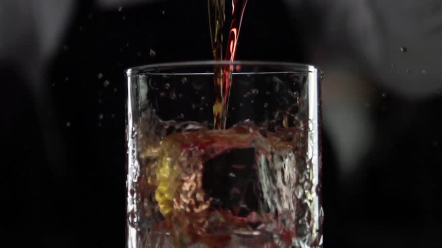 Alcohol being poured in a clear glass over large ice in slow motion