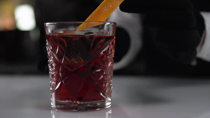 Waiter puts an orange peel in red cocktail