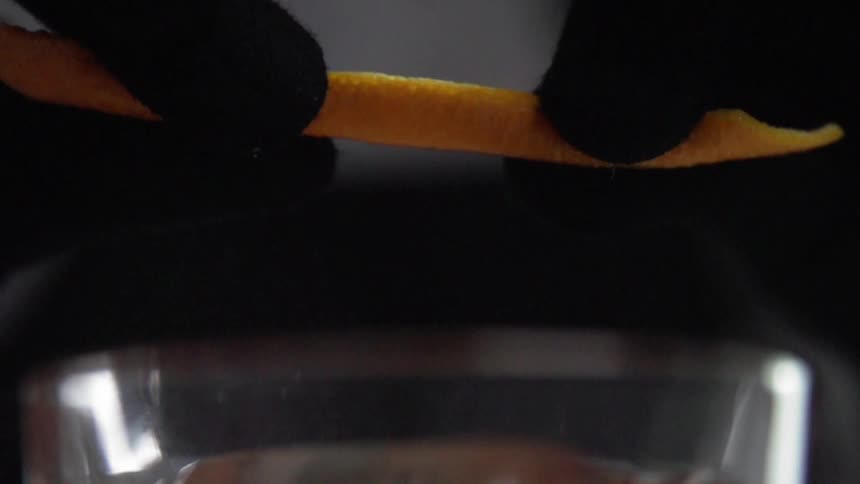 A persons hands with black gloves holding an orange peel over a glass