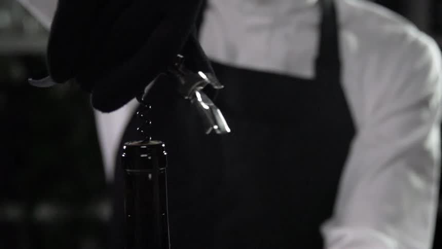 A person opens a bottle of wine with a corkscrew