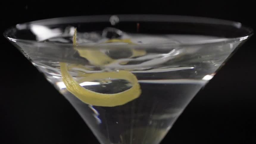 A lemon rind falls in to a martini glass with a beverage in it